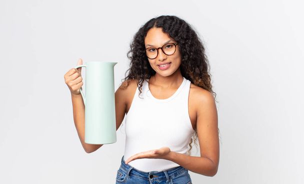 hispanic pretty woman smiling cheerfully, feeling happy and showing a concept and holding a coffee thermos - Photo, image