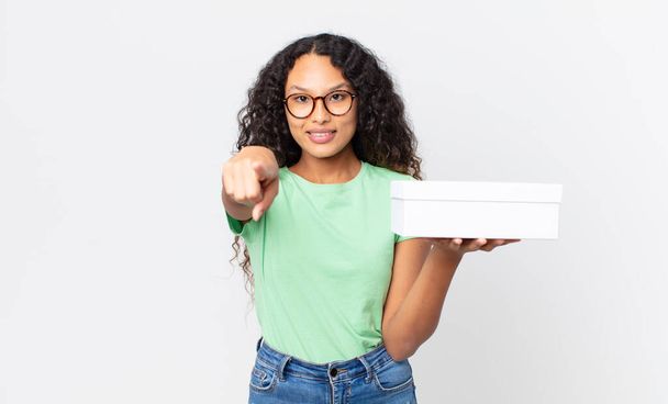 hispanic pretty woman pointing at camera choosing you and holding a white box - Foto, imagen