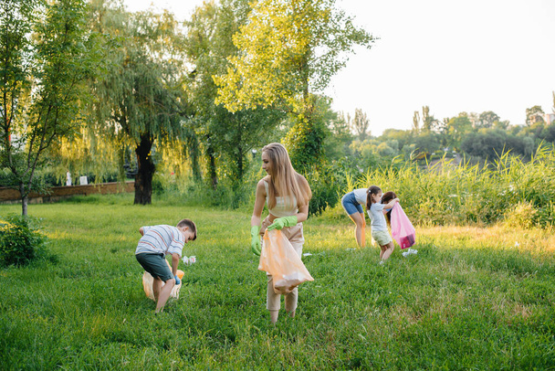 Um grupo de meninas com crianças ao pôr do sol estão envolvidas na coleta de lixo no parque. Cuidados ambientais, reciclagem. - Foto, Imagem