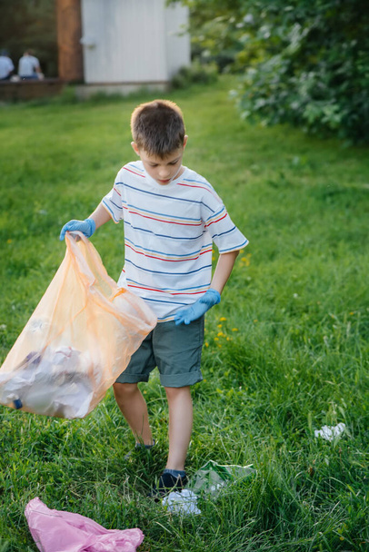 A seven-year-old boy at sunset is engaged in garbage collection in the park. Environmental care, recycling. - Fotografie, Obrázek