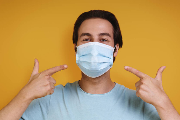 Portrait of young man in protective face mask looking at camera while standing against yellow background - Photo, image