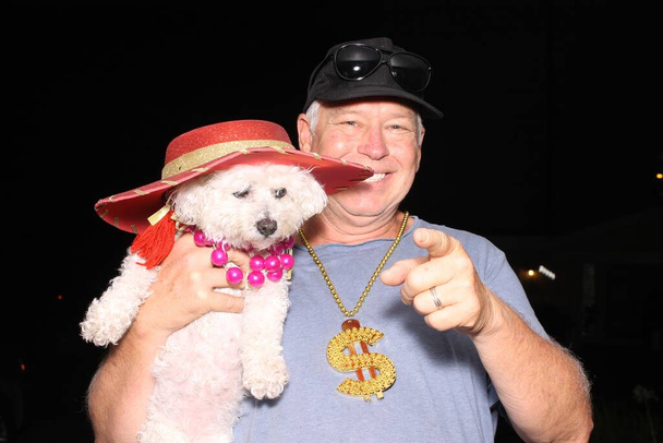 Photo Booth. A man smiles and laughs while posing with his dog for their pictures in a Photo Booth at a party. Photo Booth Party set. Glasses, hats, lips, mustaches, masks for photo booth party. Wedding Party funny pictures. Dogs Love Photo Booths.  - Photo, Image