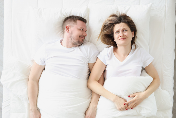 Разочарованная женщина лежит в постели с улыбающимся мужчиной крупным планом - Фото, изображение