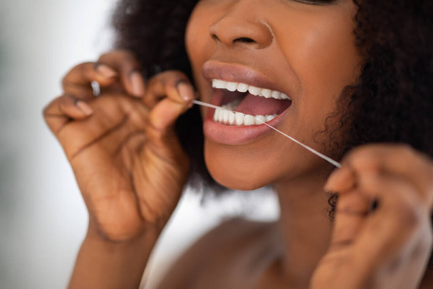 Femme afro méconnaissable nettoyant les dents avec de la soie dentaire à la maison, gros plan. Hygiène buccale, bien-être, mode de vie sain - Photo, image