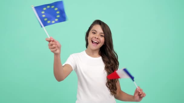szczęśliwy dziecko machając europejskimi unii i francuskiej flagi na niebieskim tle, wakacje we Francji - Materiał filmowy, wideo