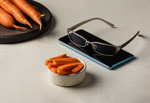 натуральный витамин А в свежей вырезанной моркови с очками на фоне телефона - Фото, изображение