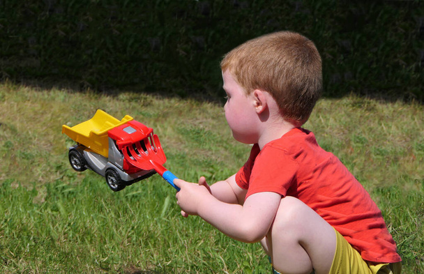 Red headed Child playing with toys in a garden - Foto, afbeelding