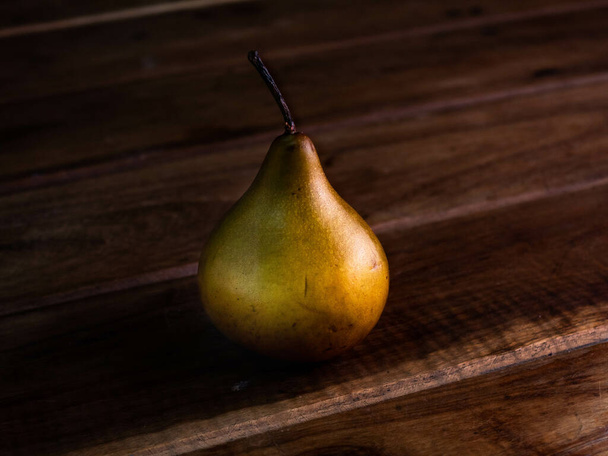 A high-angle shot of a pear on a wooden table - Zdjęcie, obraz