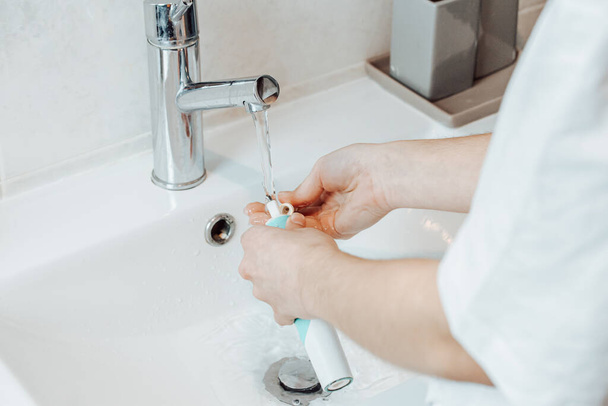 Ένα υψηλής γωνίας πλάνο των γυναικείων χεριών καθαρισμού ηλεκτρική οδοντόβουρτσα κάτω από τρεχούμενο νερό - Φωτογραφία, εικόνα