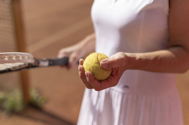 A closeup shot of a female tennis player with white sportswear holding a ball and a racket - Valokuva, kuva