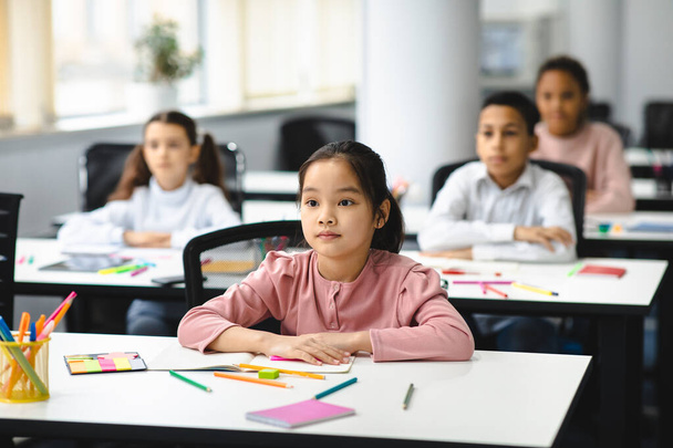 Portrait de focalisé asiatique fille assis à bureau dans salle de classe - Photo, image