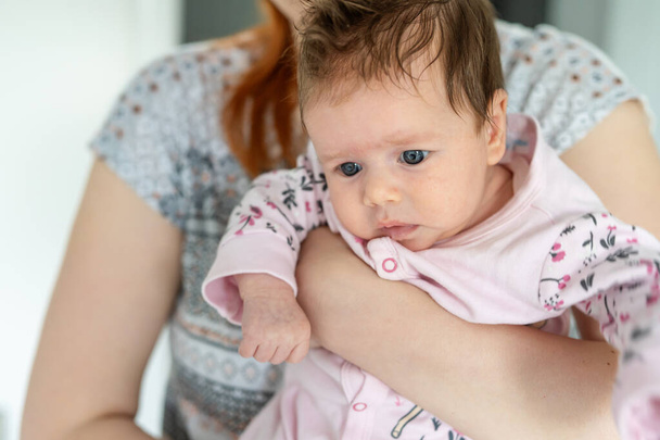 Vooraanzicht close-up portret van kleine blanke baby twee maanden oud in handen van haar moeder kijken naar de zijkant met kopieerruimte - Foto, afbeelding