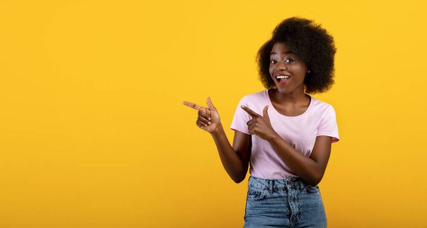 Cool offer. Cheerful african american lady pointing two fingers aside at copy space on yellow background, panorama - Фото, изображение