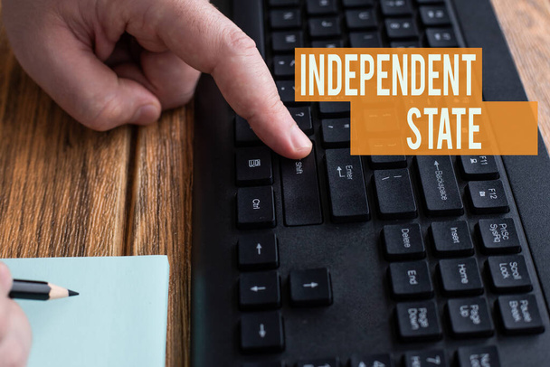 Text sign showing Independent State. Business approach ability of the state to be independent and have autonomy Hands Pressing Computer Keyboard Keys While Writing With Pencil In Notepad. - Photo, image