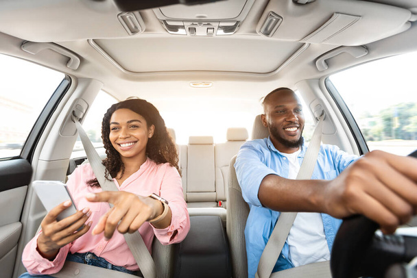 Happy black couple driving car and using cell phone - Foto, Imagem