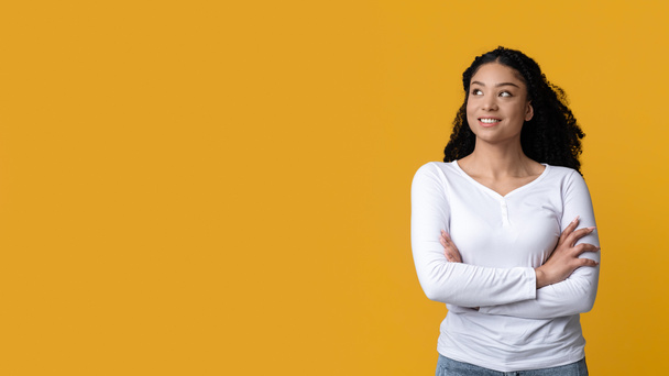 Dreamy Young African American Woman Standing With Folded Arms Over Yellow Background - Foto, immagini