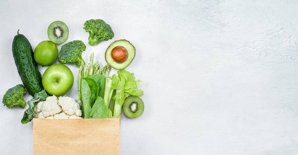 green vegetables and fruits in a paper bag on a light gray background - Foto, immagini