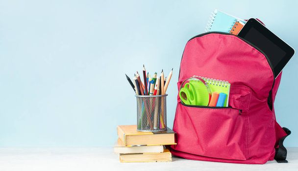 mochila con útiles escolares, libros y portalápices sobre un fondo azul claro - Foto, Imagen