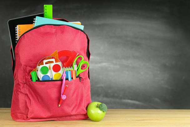 jeden czerwony plecak szkolny i zielone jabłko na stole na tle tablicy - Zdjęcie, obraz
