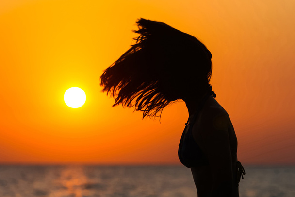 Νεαρή γυναίκα πετώντας μαλλιά στο ηλιοβασίλεμα - Φωτογραφία, εικόνα