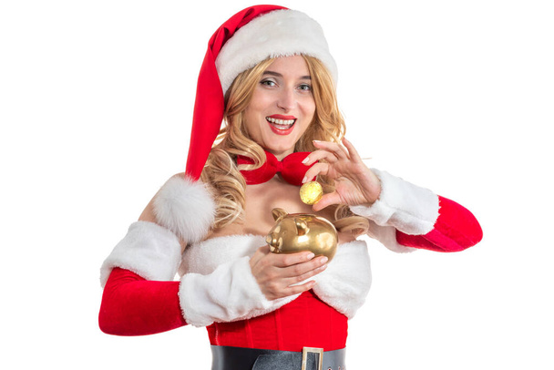Леді Санта Клаус щасливо посміхається з монетою і золотим голубиним банком. Красуня в червоній сукні, біле хутро. Весела дівчина у капелюсі Санти. Жінка дивиться на різдвяну вечірку, косплей, святковий маскарад, карнавал. - Фото, зображення