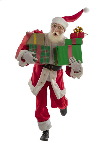 Santa Claus sobre fondo blanco aislado. Hombre mayor actor viejo con una barba blanca real en el papel de Papá Noel trayendo cajas envueltas regalos de Navidad. Deprisa, tarde, bailando, saltando, corriendo. - Foto, Imagen