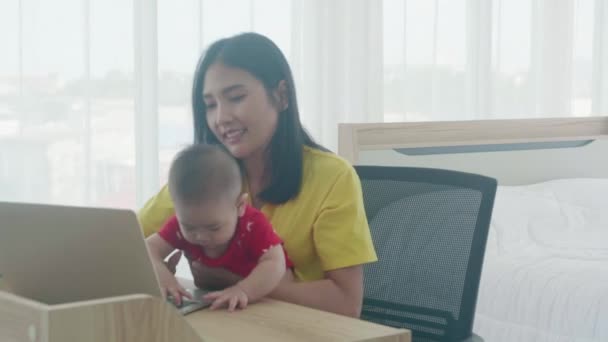 Onnellinen perhe, jossa äiti kantaa vauvaa ja työskentelee kannettavalla tietokoneella internetiin verkossa kotona, äiti, jolla on tytär, joka käyttää muistikirjaa ammattimaisesti, liike- ja työkonsepteilla. - Materiaali, video