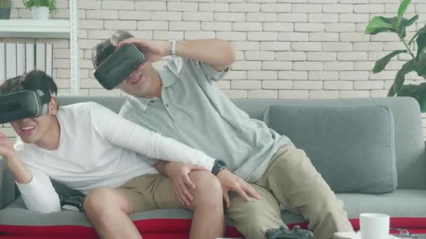 Счастливая семья с сыном и отцом играют в видеоигру VR-гарнитуры с возбуждением и весельем вместе на диване дома, пожилые и молодые люди активно используют виртуальную реальность с развлечениями. - Кадры, видео