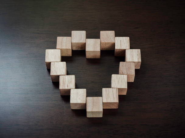 Bloques de madera dispuestos en forma de corazón sobre fondo de madera oscura, vista superior. Concepto de amor y convivencia. - Foto, Imagen