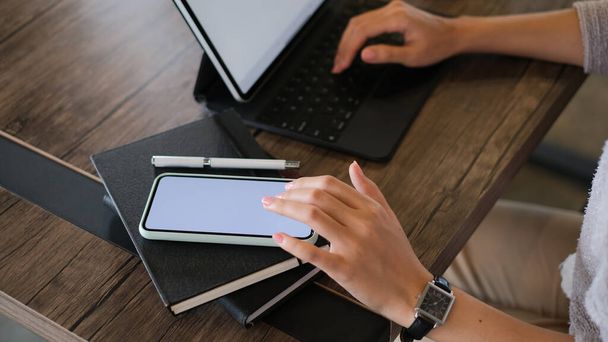 Обрезанный снимок женщины с помощью мобильного телефона с пустым экраном и просмотр Интернета на планшетном компьютере в офисе. - Фото, изображение
