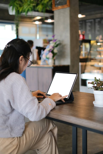Achteraanzicht van een jonge zakenvrouw werkt met computer tablet in modern café. - Foto, afbeelding