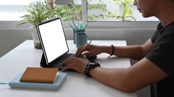 Skoncentrowany młody człowiek freelancer pracuje na tablecie z pustym ekranem siedząc w miejscu pracy. - Zdjęcie, obraz