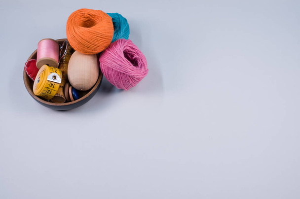 A bowl of sewing accessories and colorful textile balls of wool on gray background with a copy space - Fotó, kép
