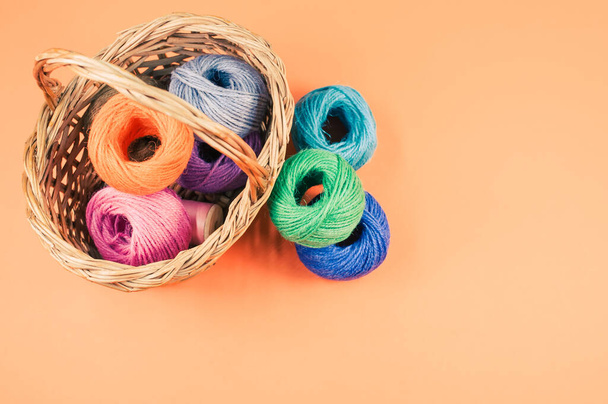 A pile of colorful textile balls of wool in a wicker basket on orange background with a copy space - Photo, Image