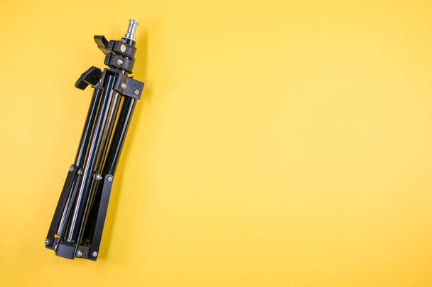 A closeup shot of a black iron folding tripod on a yellow background with a copy space - Foto, Imagen