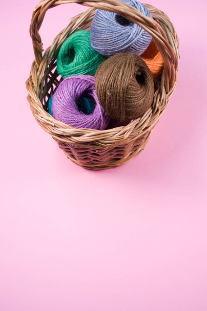A pile of colorful textile balls of wool in a wicker basket on pink background with a copy space - Foto, Bild