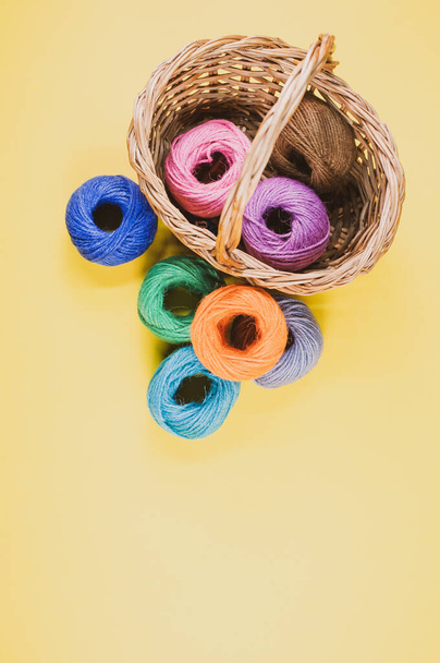A pile of colorful textile balls of wool in a wicker basket on yellow background with a copy space - Foto, Bild
