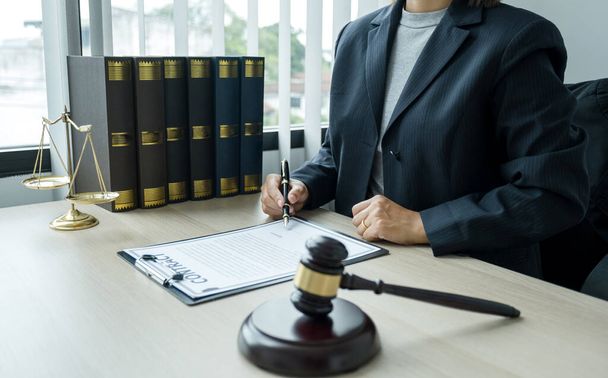Prawniczka siedzi przy biurku z młotkiem i skalą sprawiedliwości. Badanie prawa w sporach biznesowych w celu udzielania porad klientom. - Zdjęcie, obraz