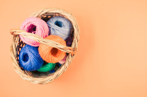 A pile of colorful textile balls of wool in a wicker basket on orange background with a copy space - Foto, immagini