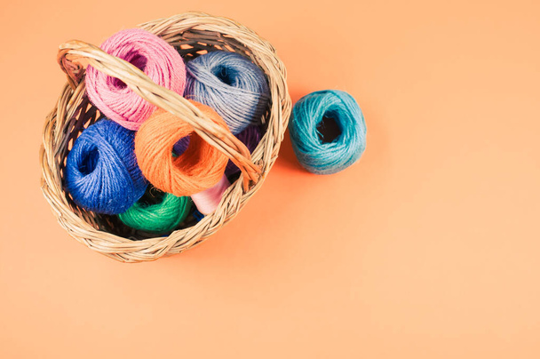 A pile of colorful textile balls of wool in a wicker basket on orange background with a copy space - Φωτογραφία, εικόνα