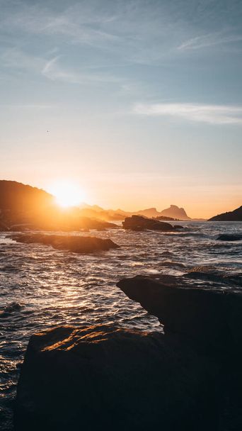 A vertical shot of a beautiful sunrise behind the rocks at sea - 写真・画像