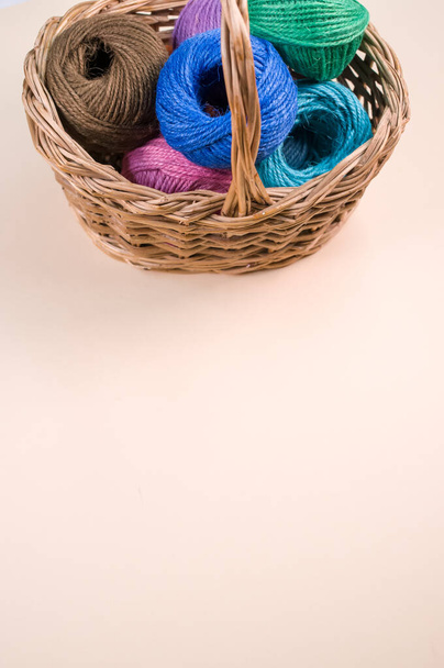A pile of colorful textile balls of wool in a wicker basket on brown background with a copy space - Foto, Bild