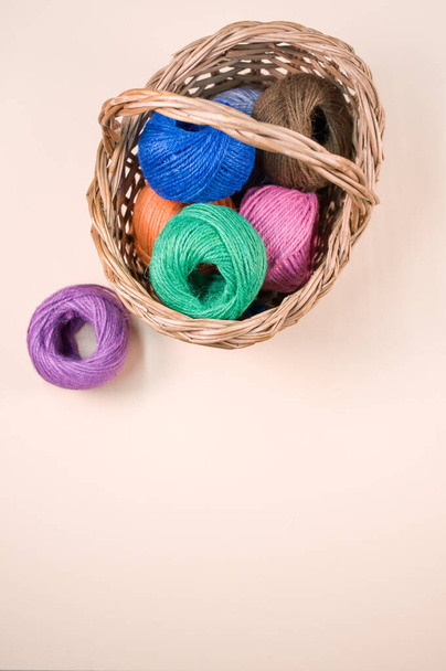 A pile of colorful textile balls of wool in a wicker basket on brown background with a copy space - Fotó, kép