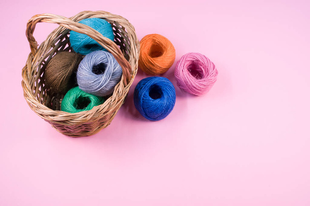A pile of colorful textile balls of wool in a wicker basket on pink background with a copy space - Foto, afbeelding