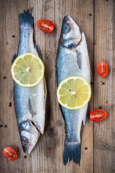 Due pesce crudo di mare con limone e pomodorini su ba di legno
 - Foto, immagini