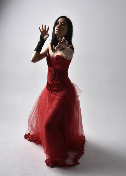 Retrato de larga duración de una hermosa joven asiática con corsé rojo y corona de reina gótica adornada. Elegante de pie posando aislado en el fondo del estudio. - Foto, imagen