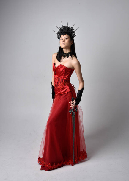 Ritratto a figura intera di bella giovane donna asiatica che indossa corsetto rosso e ornata corona regina gotica. grazioso in piedi posa isolato su studio sfondo. - Foto, immagini