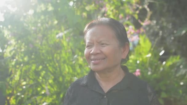 笑顔アジアの高齢者の祖母は、自宅で朝の日差しの下で庭で彼女の愛らしい孫娘を喜んで抱きしめています。２人で。愛だ。家族の中で二世代の絆. - 映像、動画