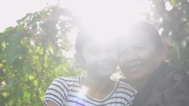 Asiática feliz abuela mayor y adorable nieta adolescente posando abrazos entre sí y mirando a la cámara en el jardín en casa bajo la luz del sol de la mañana. Relación de unión en familia. - Metraje, vídeo