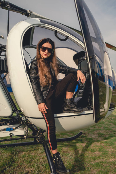 Між дівчиною в сонцезахисних окулярах сидить у відкритій кабіні вертольота
 - Фото, зображення